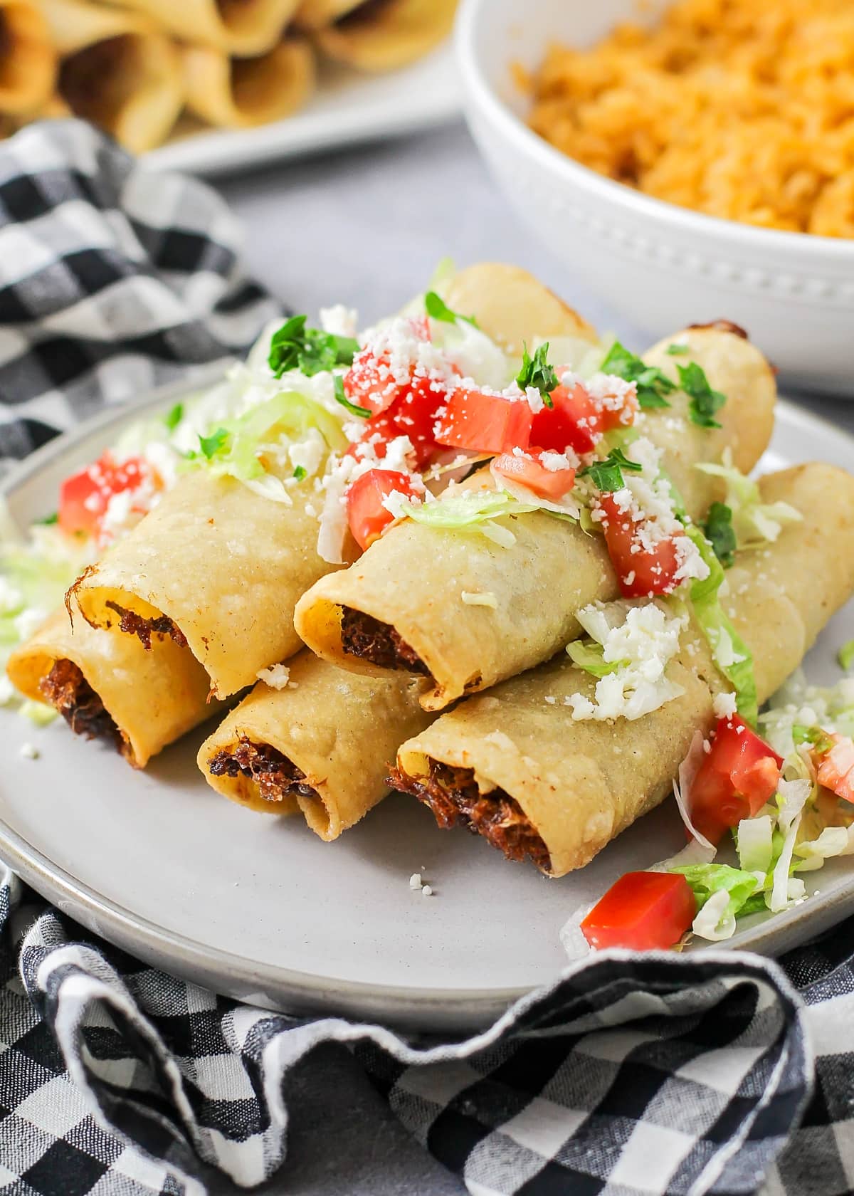 Flautas recipe with fresh guacamole and diced tomatoes on a plate.