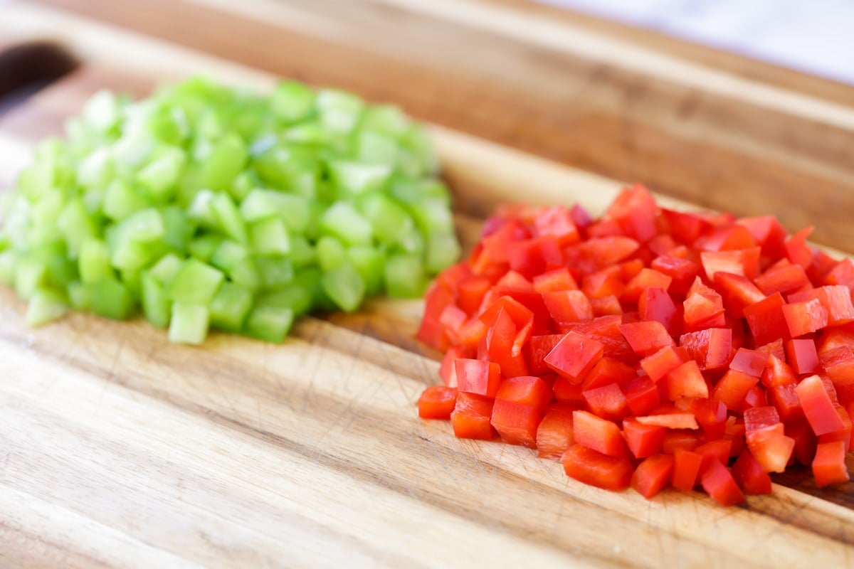 Red and green peppers diced on a cutting board.