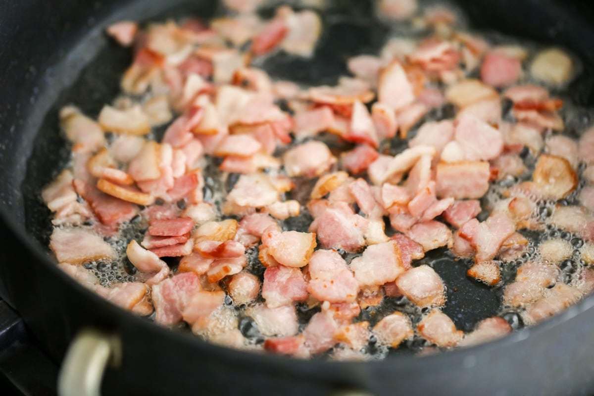 Diced bacon frying in a pan on the stove.
