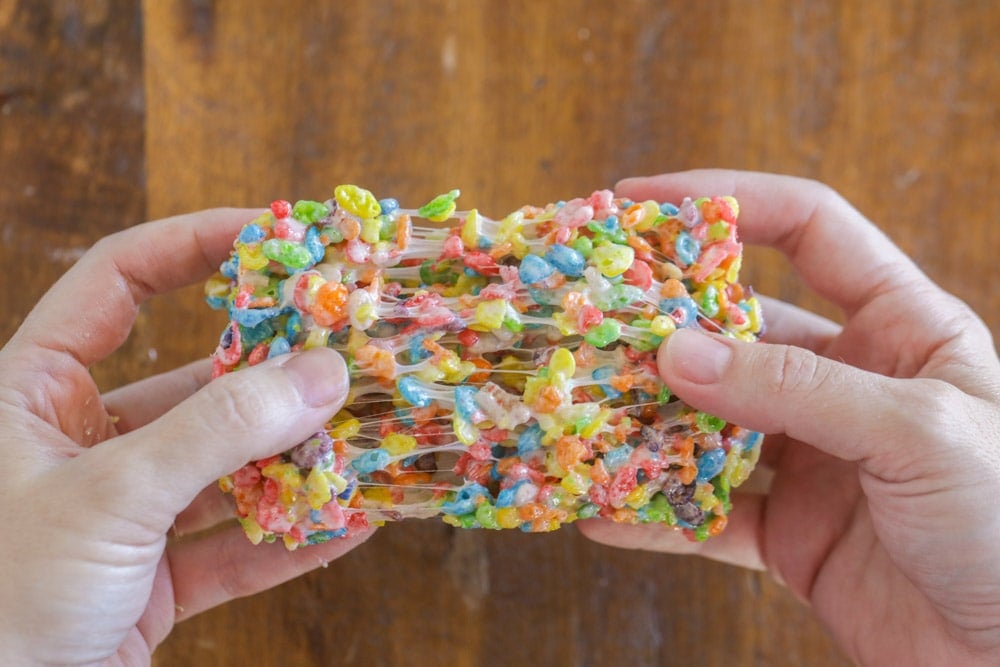 Fruity Pebbles treats being pulled apart over wood table.