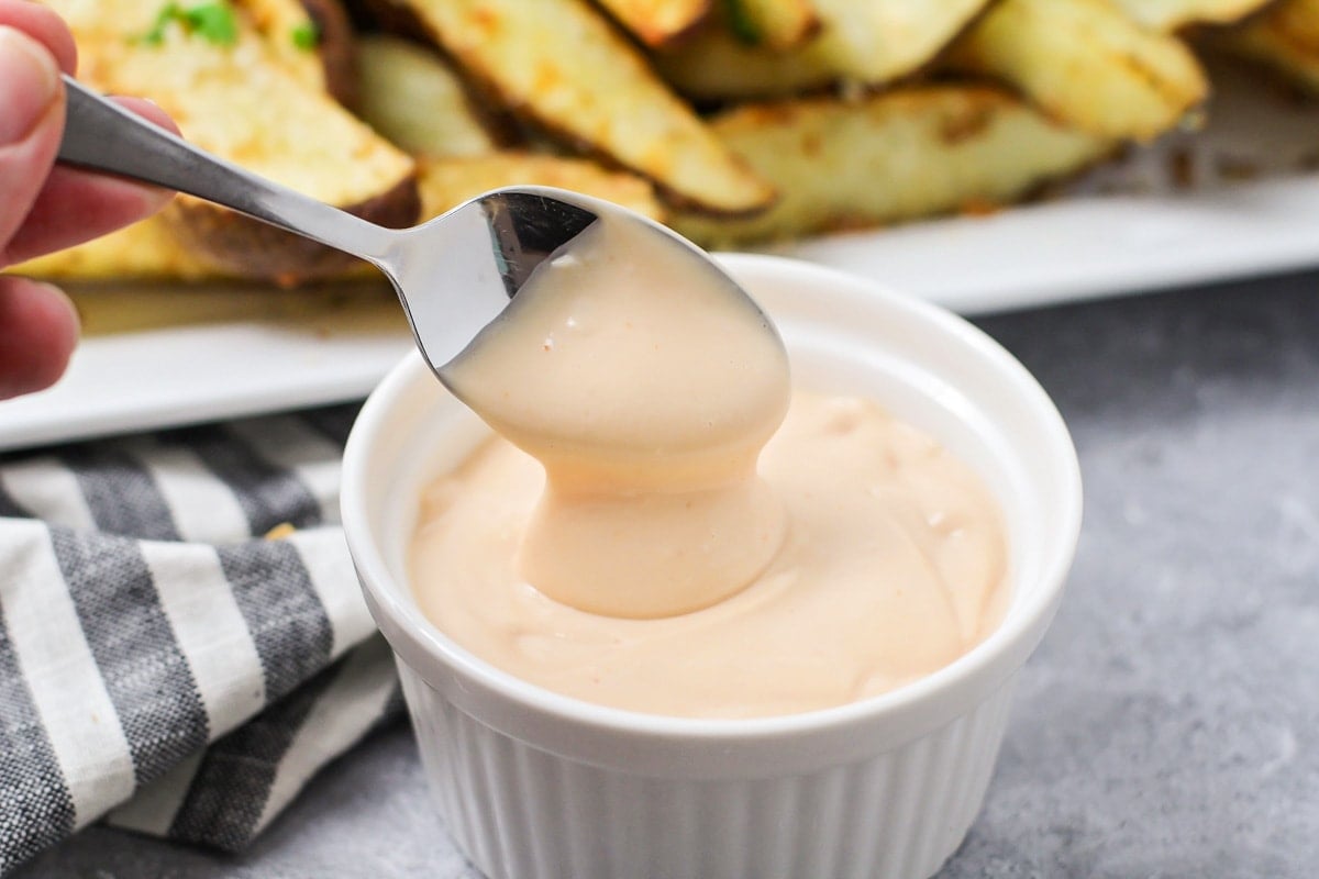 A metal spoon dipped in a white ramekin filled with fry sauce.