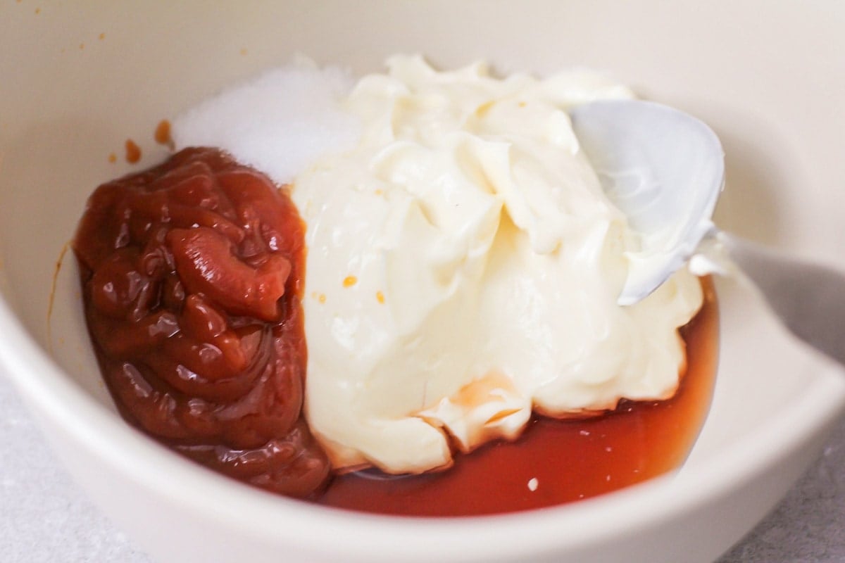 Mixing ketchup, mayonnaise, worcestershire sauce, and red wine vinegar together in a white bowl.