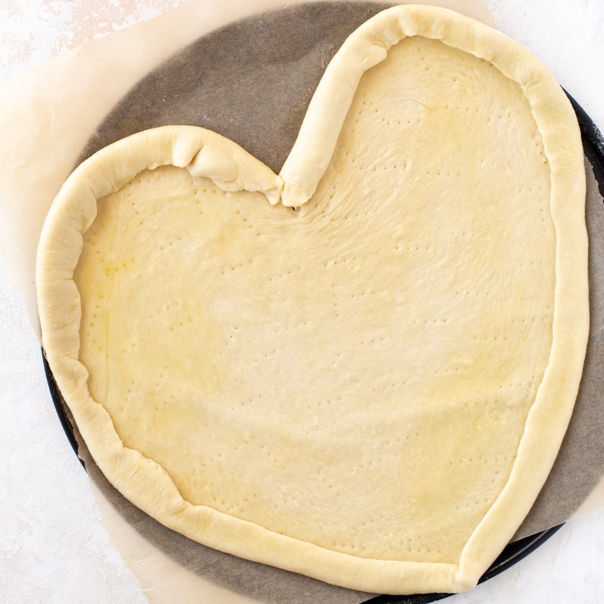 Pizza dough shaped like a heart and rolled on a baking pan.