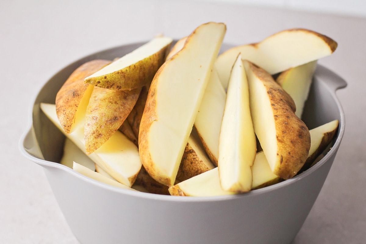 Uncooked potato wedges in a gray mixing bowl.