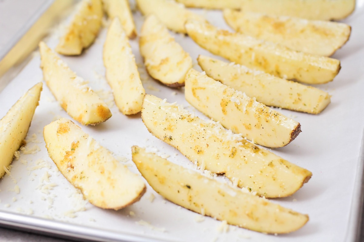 Seasoned potato wedges in a parchment lined baking sheet.
