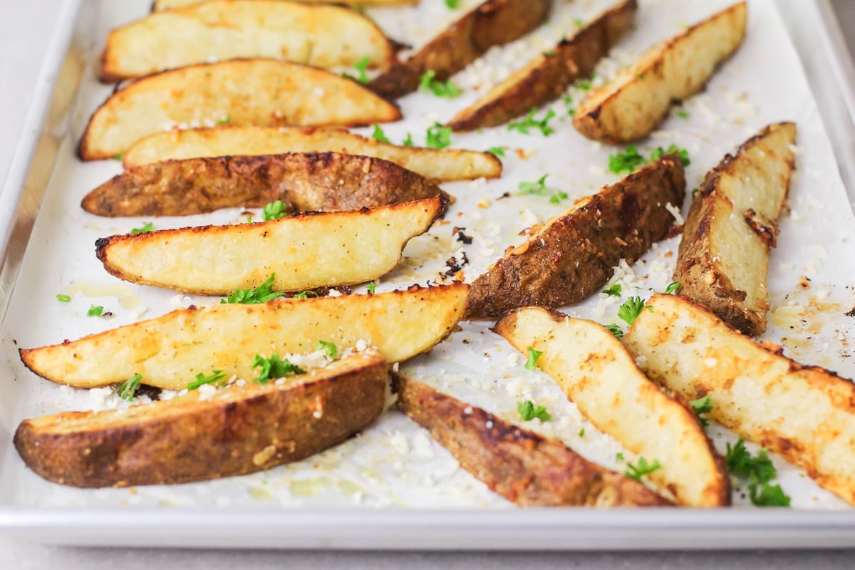 Cooked potato wedges on a parchment lined baking sheet.