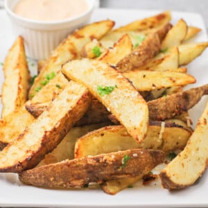 Potato wedges on a white plate served with dipping sauce.