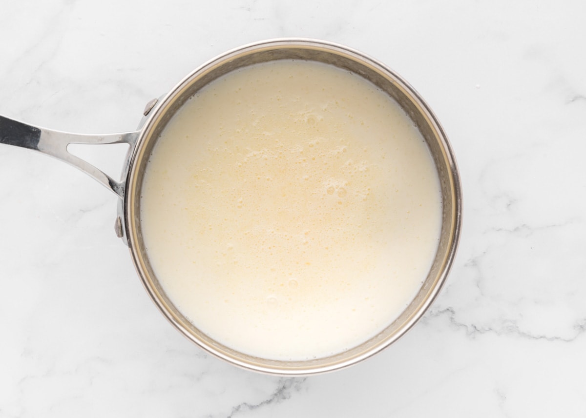Adding milk to a pot of roux in a pot.