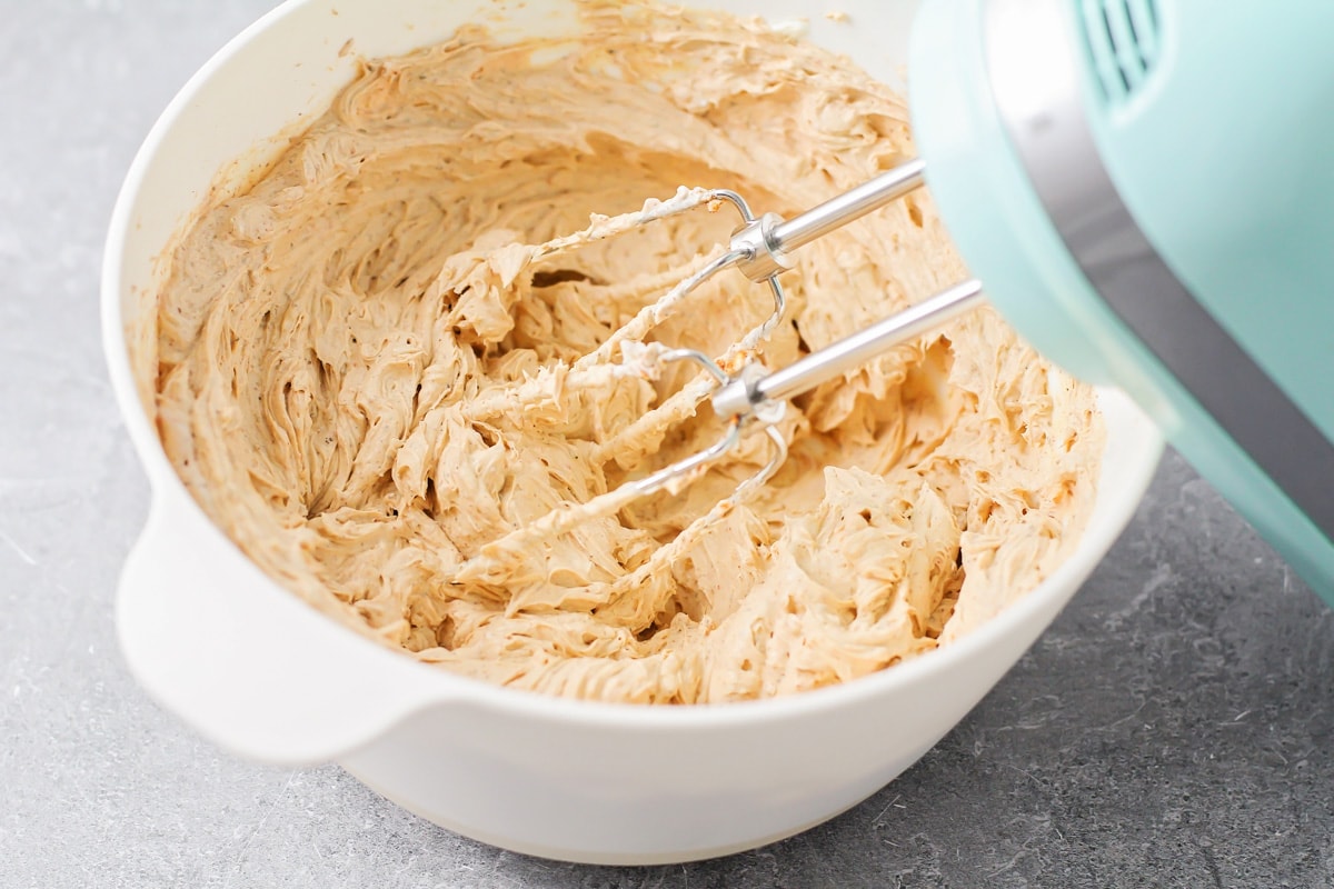 Mixing cream cheese and seasonings in a white bowl with a hand mixer.