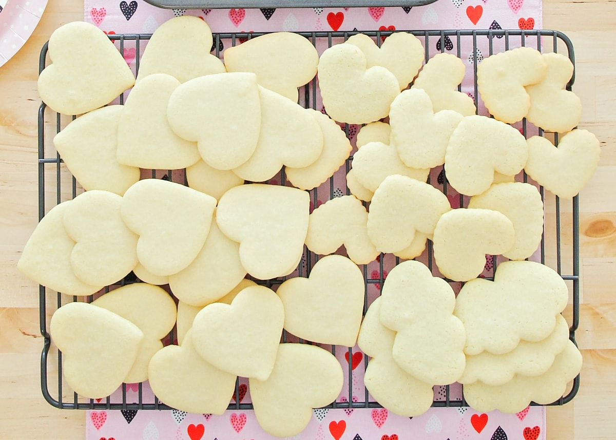 Heart shaped Valentine sugar cookies stacked on cooling rack.