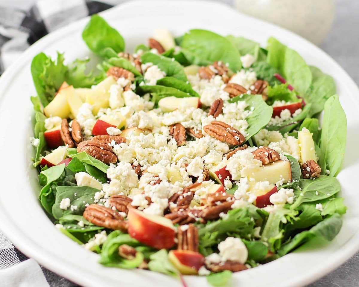Topped with a poppyseed dressing, fresh apple pecan salad is a delectable combination of flavors and textures. Close up of apple pecan salad served in a white bowl.