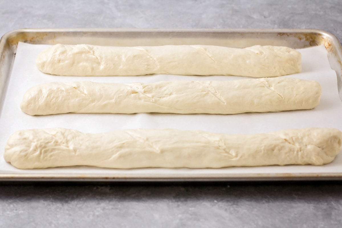 Three baguettes rolled and shaped on a lined baking sheet.