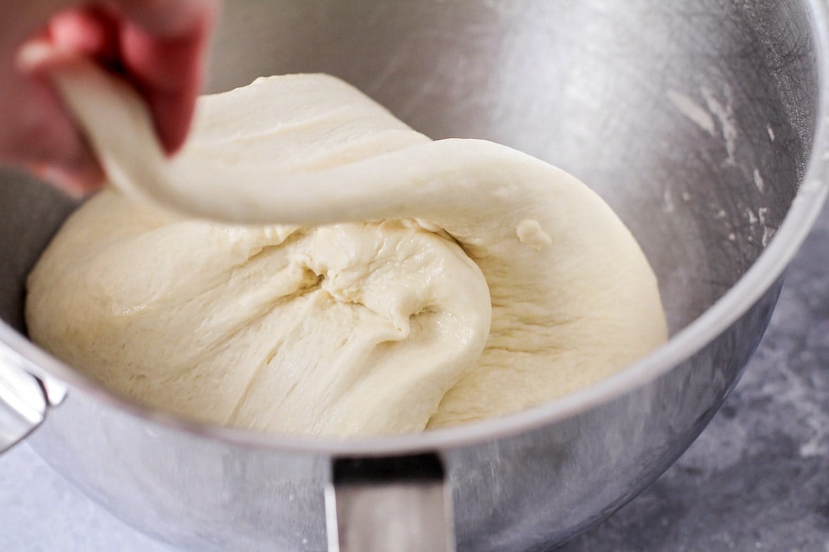 Folding bread dough onto itself in a metal bowl.