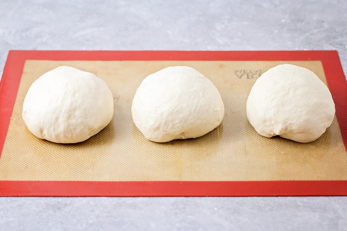 Three round balls of dough on a silpat mat.