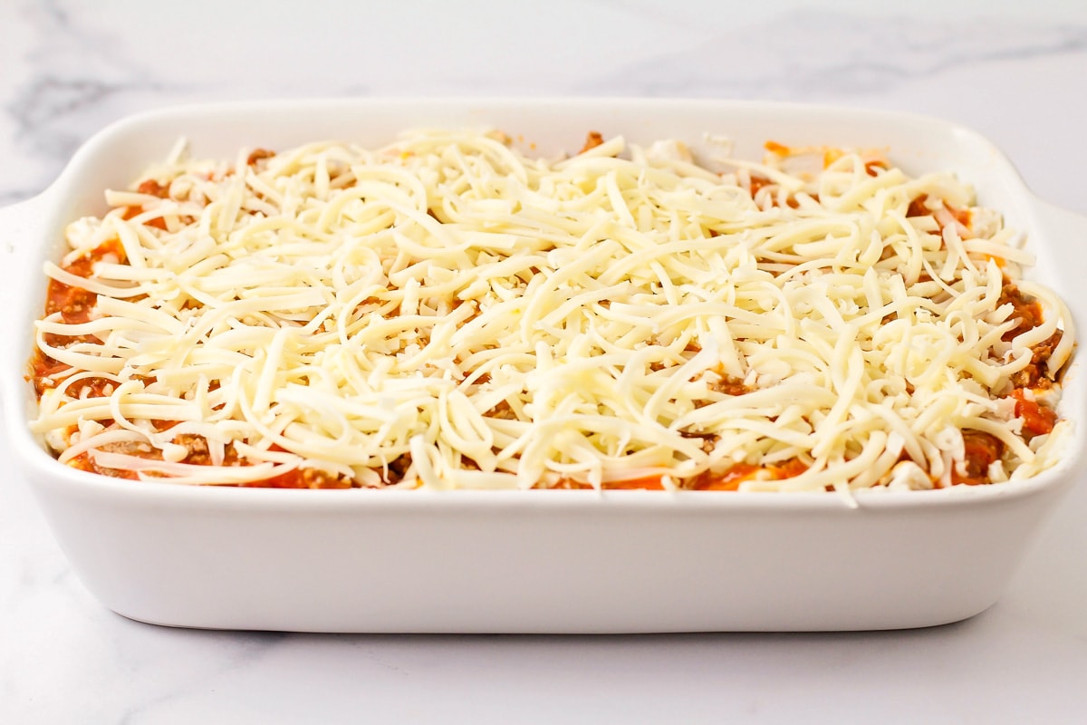 Sprinkling cheese on top of the layered pasta dish.