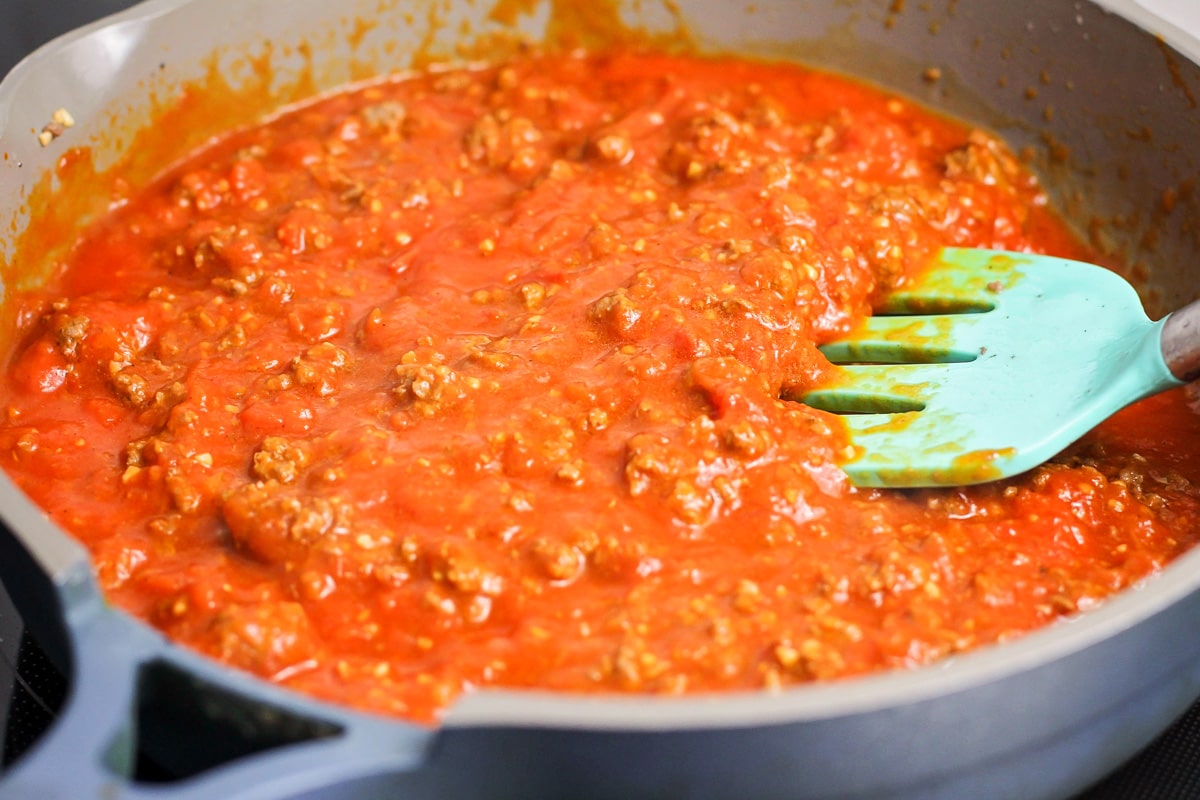 Adding marinara to the ground beef in a pot on the stove.