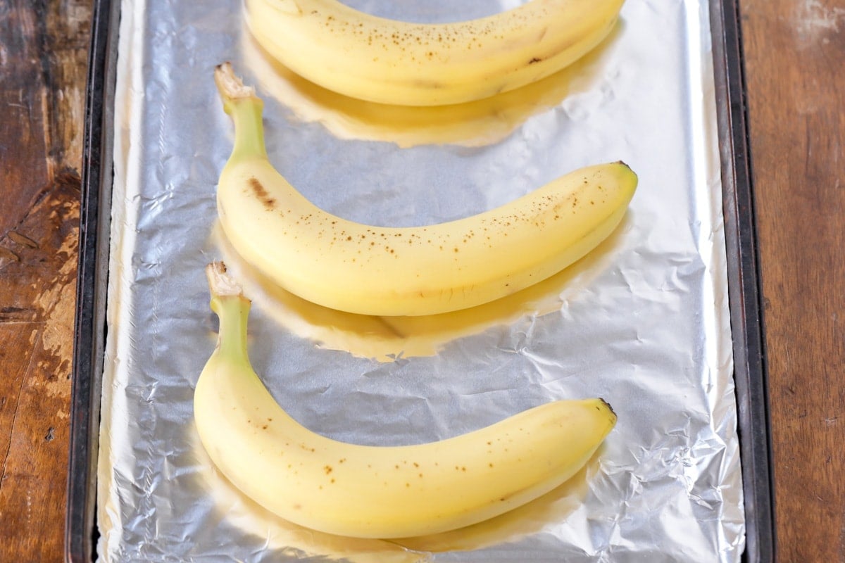 Three bananas on a tin foiled lined baking sheet.