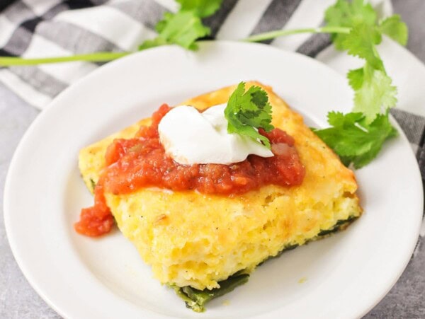 A slice of chile relleno casserole topped with fresh salsa, sour cream, and cilantro.