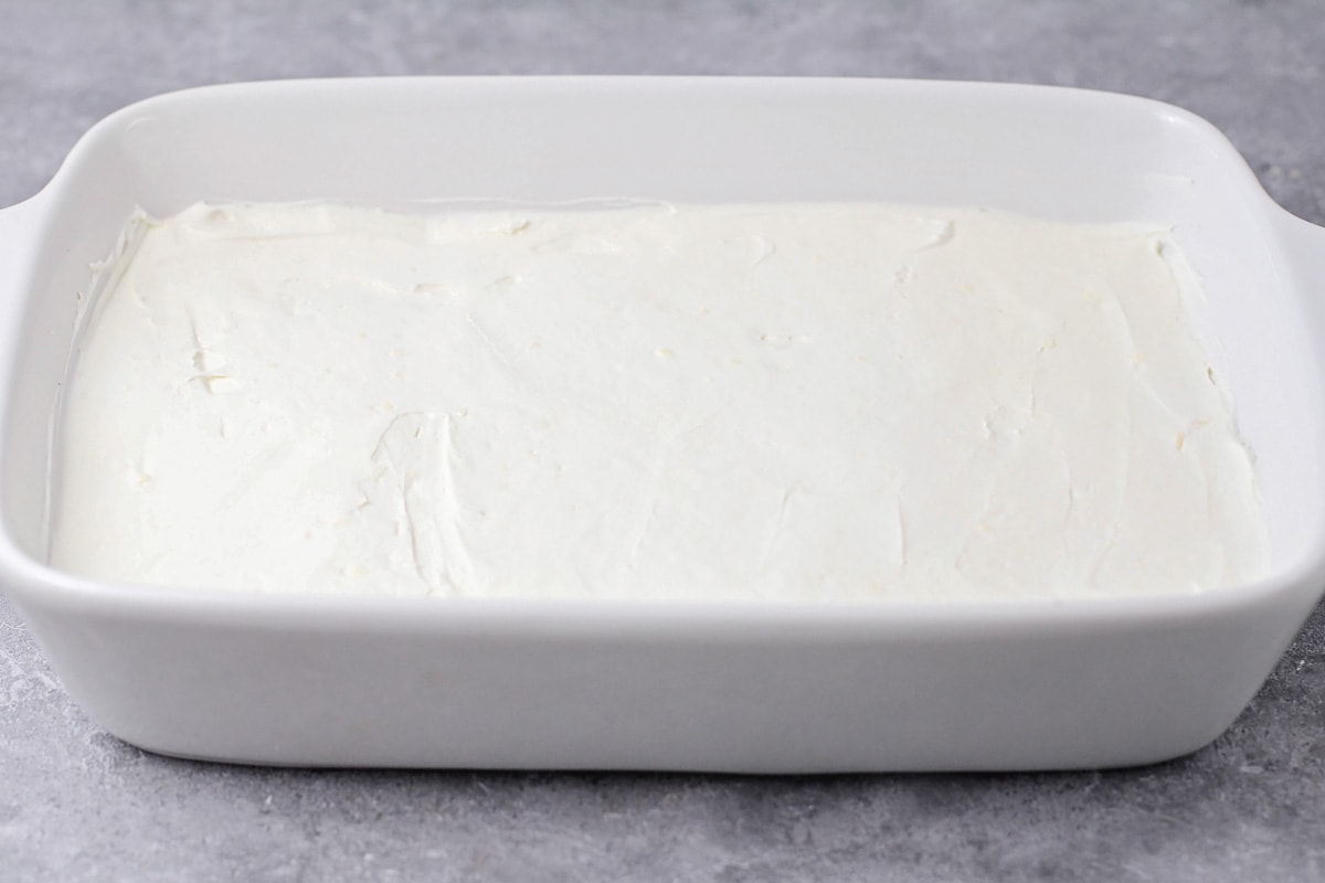 Spreading a cream cheese layer in a white baking dish.