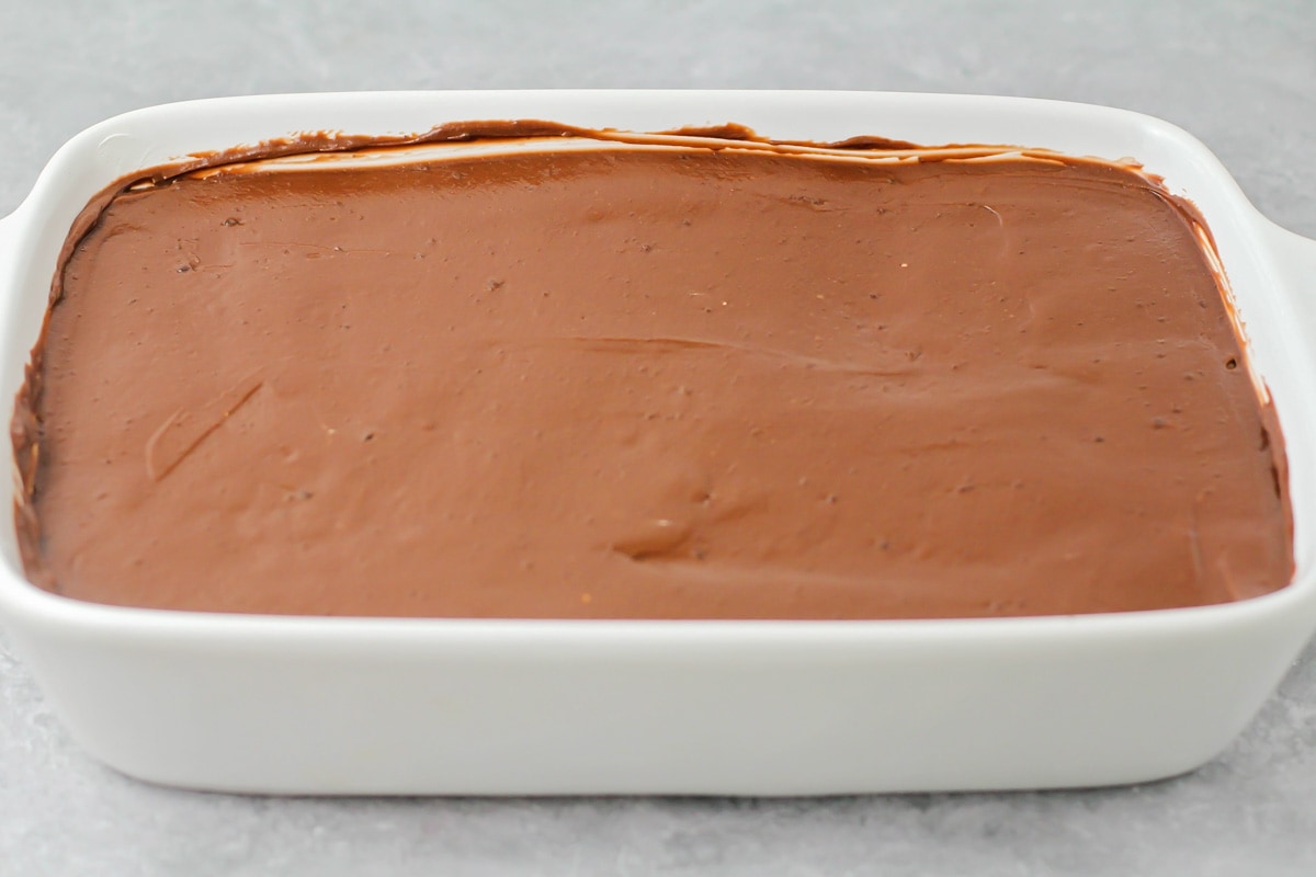 Spreading a chocolate pudding layer in a white baking dish.