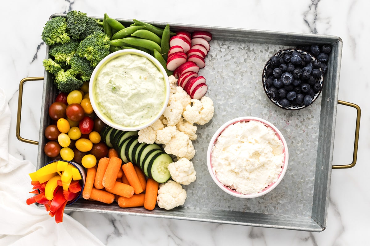 Adding more veggies to a charcuterie board with dips and blueberries.