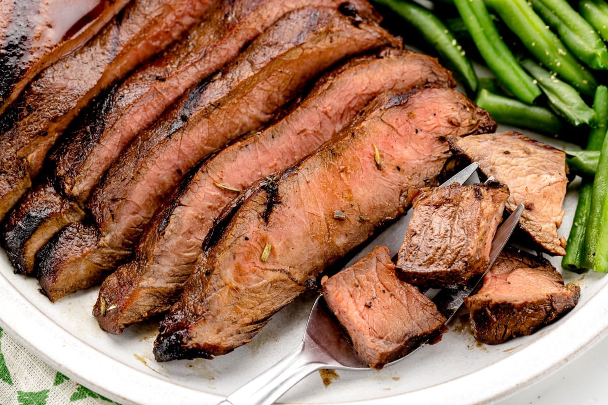 Close up of a cut steak on a white plate with green beans.