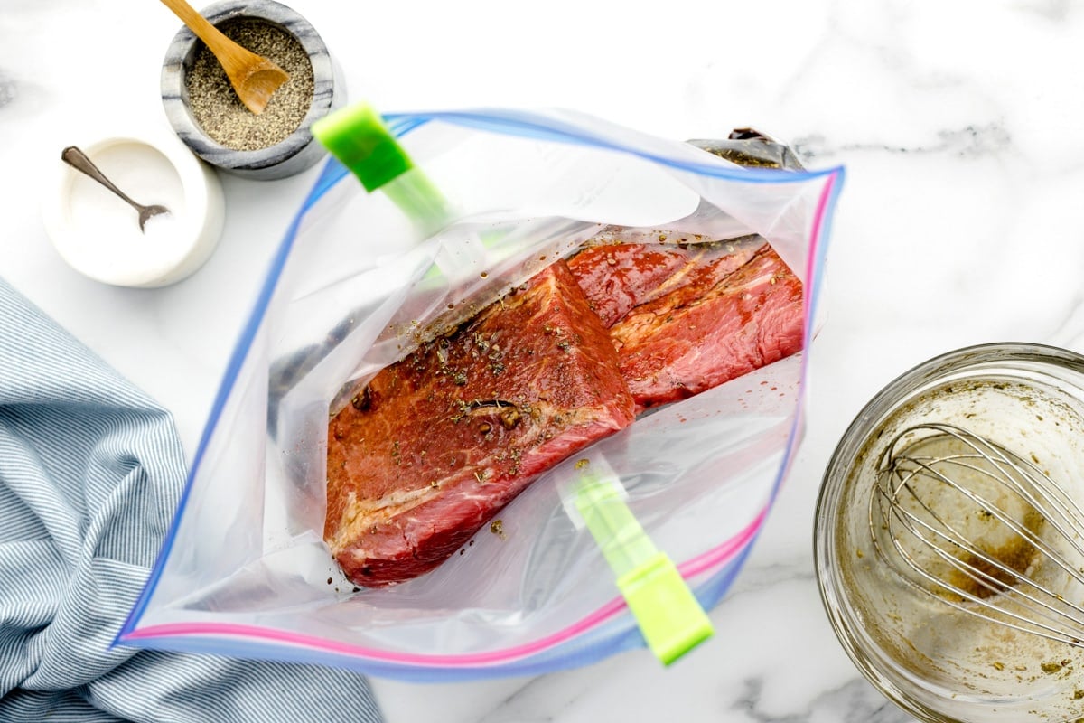 Covering a steak in marinade in a ziploc bag.