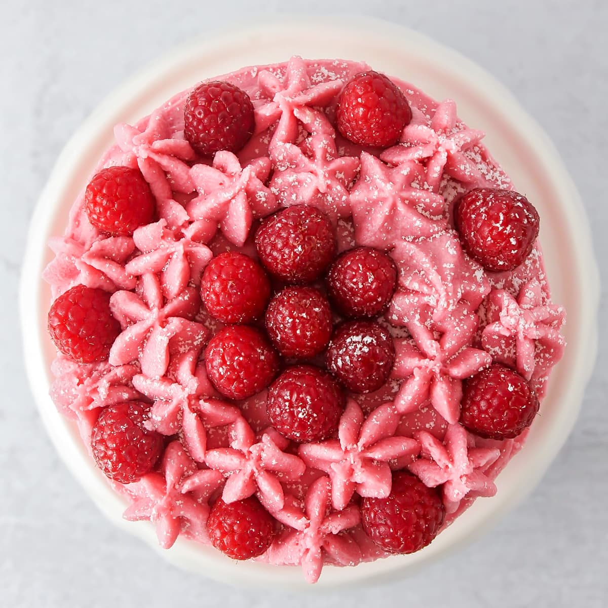 Top view of a cake decorated with raspberry buttercream frosting and fresh raspberries.