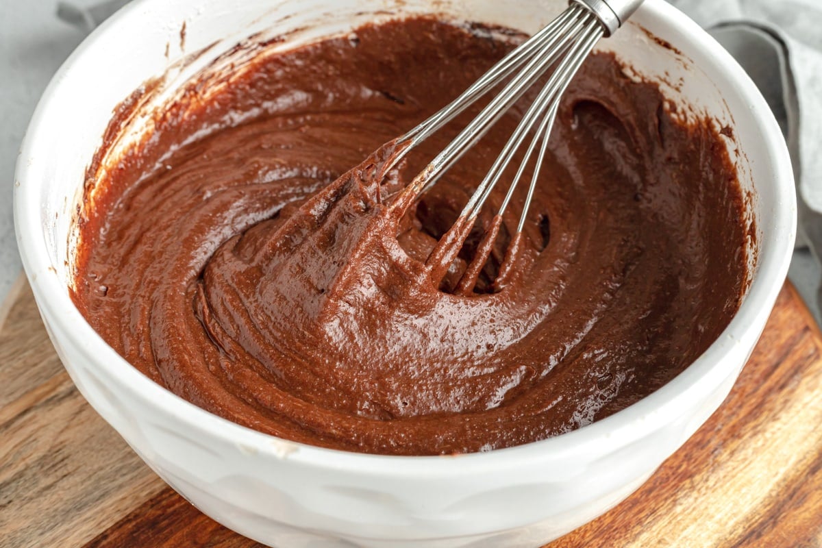 Whisking brownie batter in a white bowl.