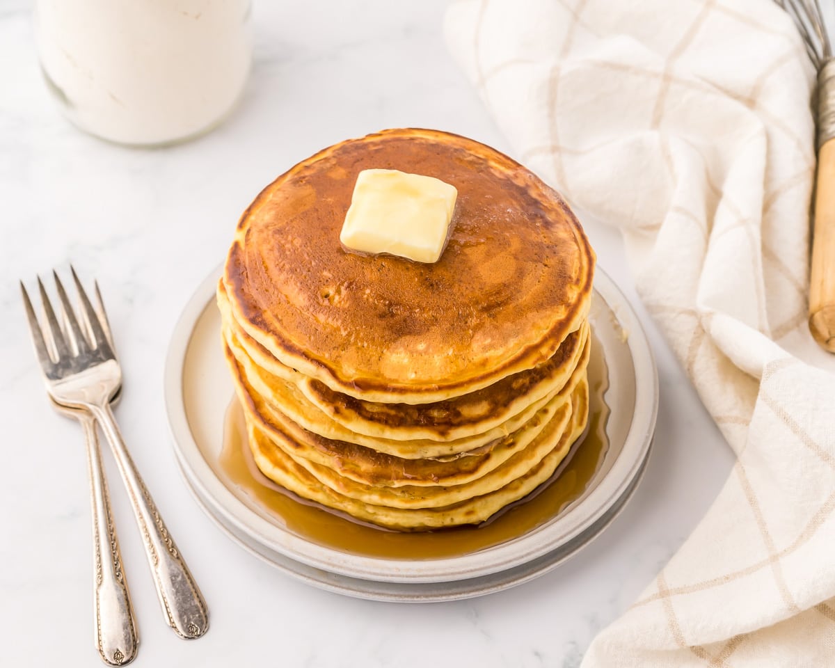 A stack of pancakes covered in maple syrup and butter on a plate.