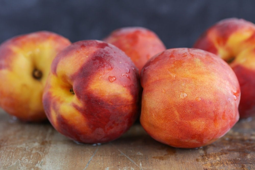 Several washed peaches on a wooden table.
