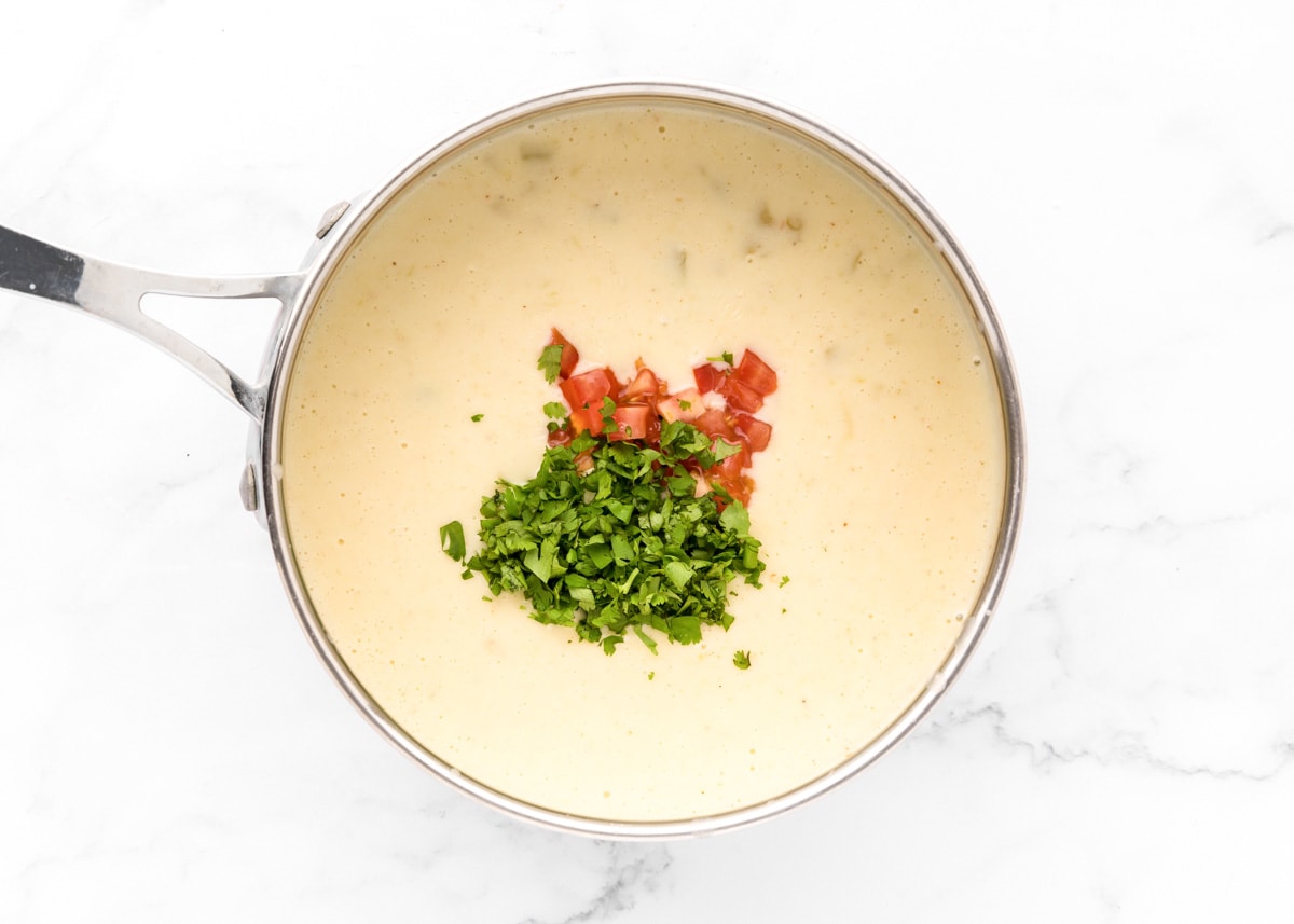 Adding chopped tomatoes and cilantro to a cheese mixture.