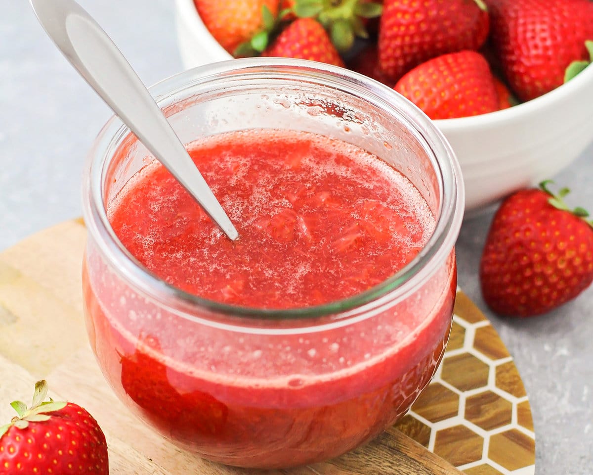 A glass jar filled with strawberry sauce.