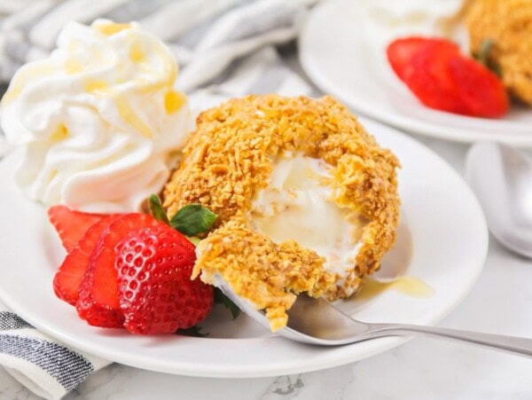 Mexican fried ice cream on white plate with strawberries and whipped cream.