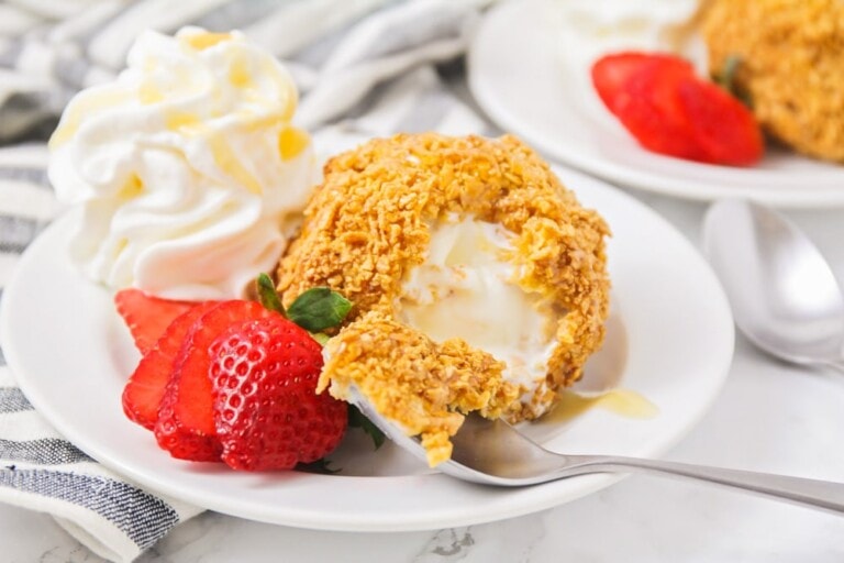 Mexican fried ice cream on white plate with strawberries and whipped cream.