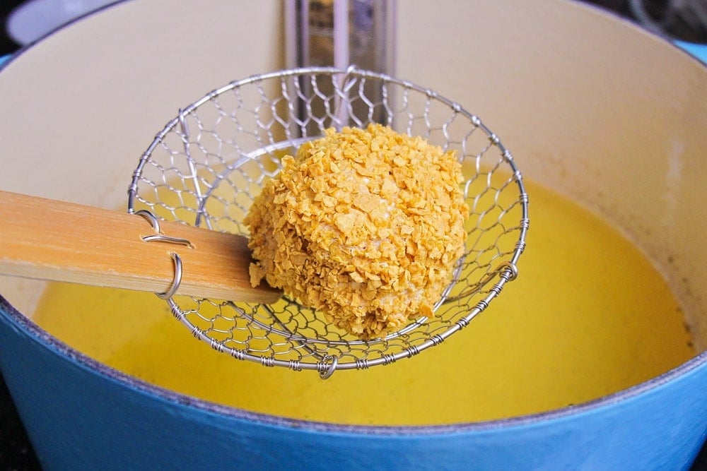 Using a strainer to place a ball of coated ice cream in a pan of oil.