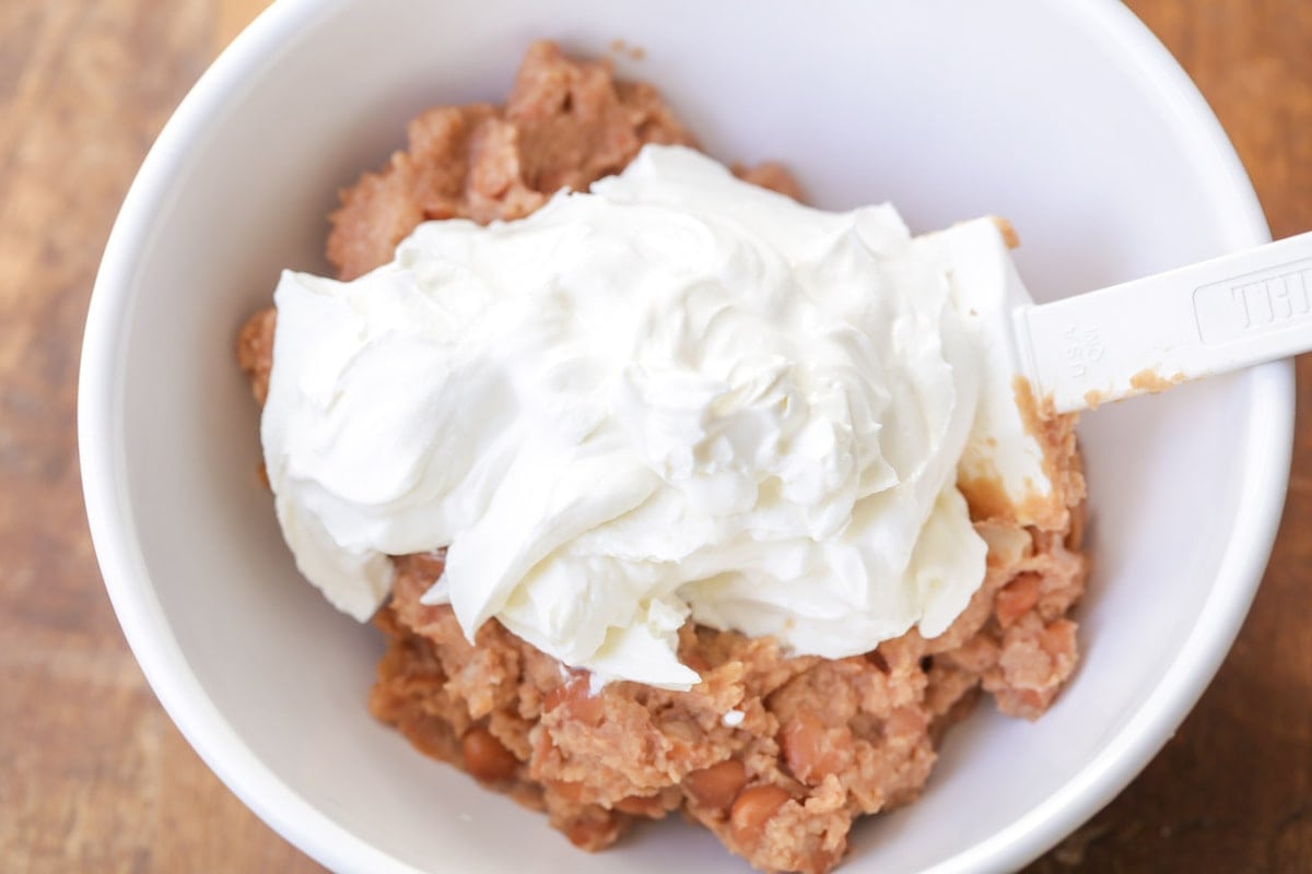 Combining cream cheese and refried beans in a white bowl.