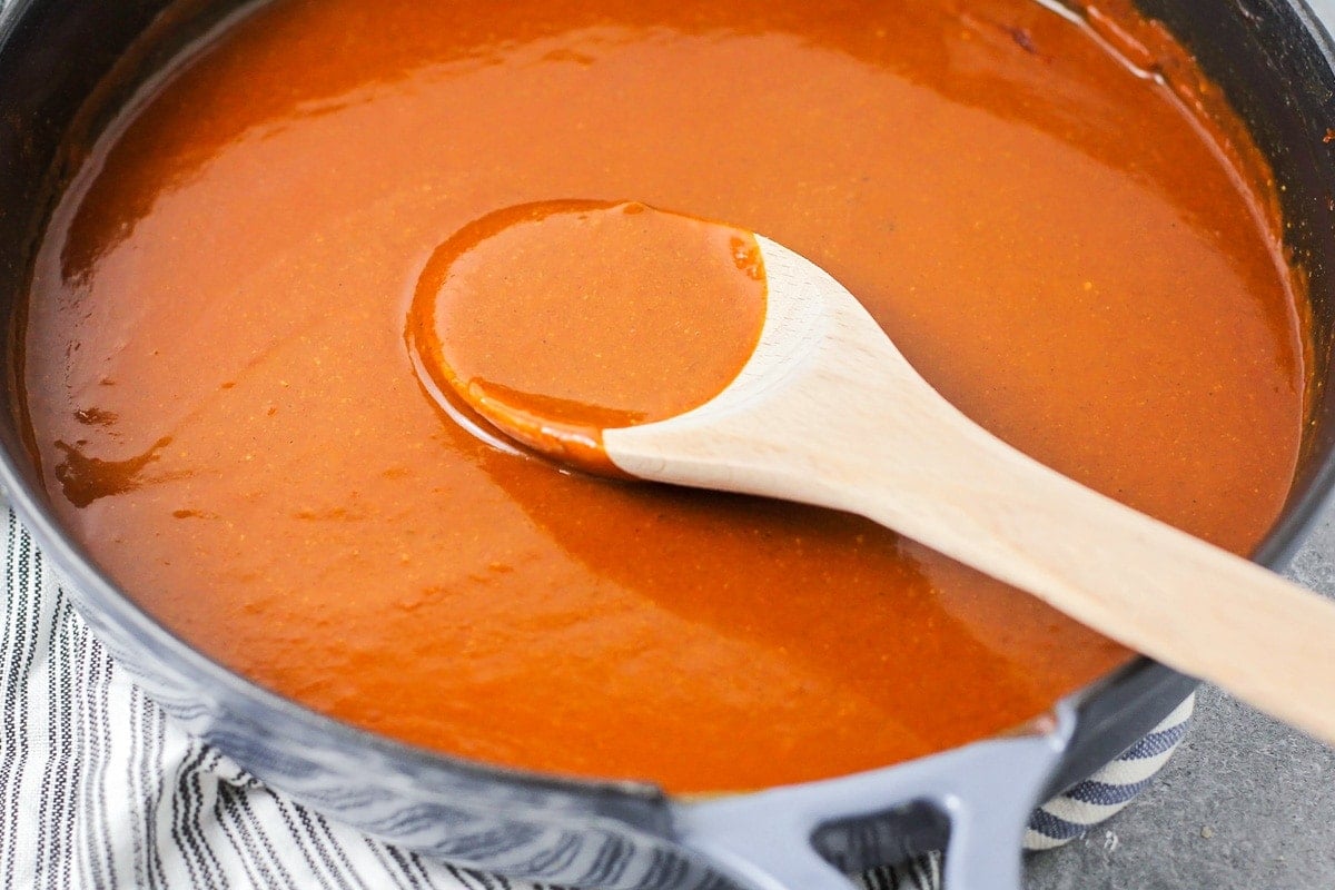 Mixing homemade red enchilada sauce in a skillet with a wooden spoon.
