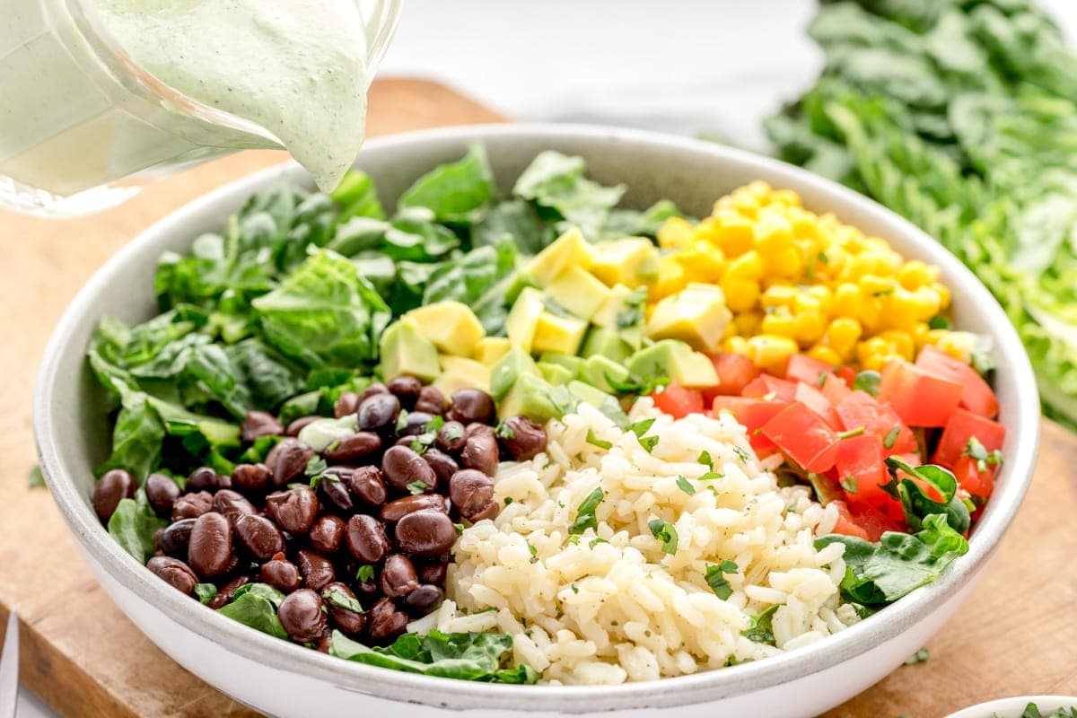 Pouring dressing onto a bowl of rice topped with beans, rice, and veggies.