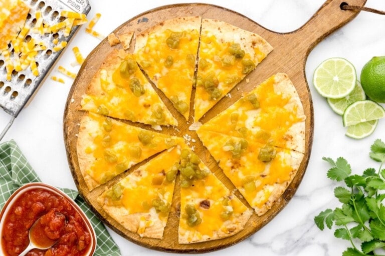 A sliced cheese crisp topped with green chilis.