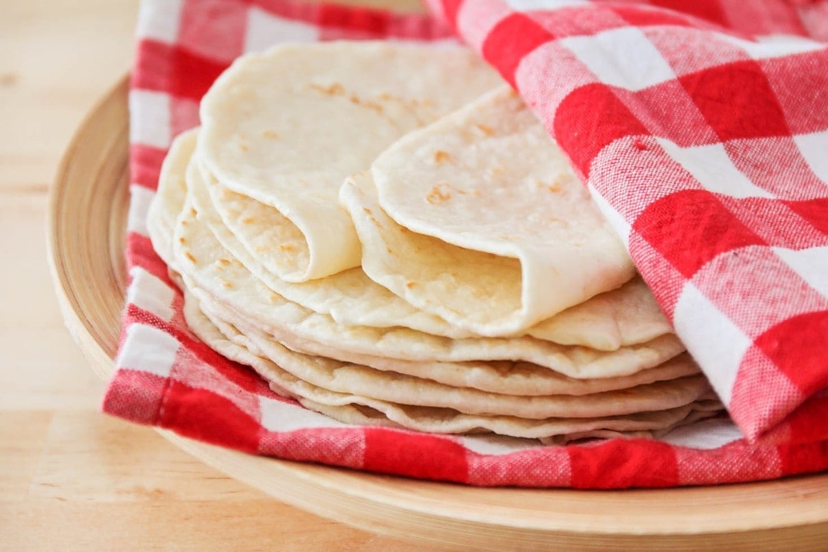 Homemade flour tortillas in a red and white checked towel.