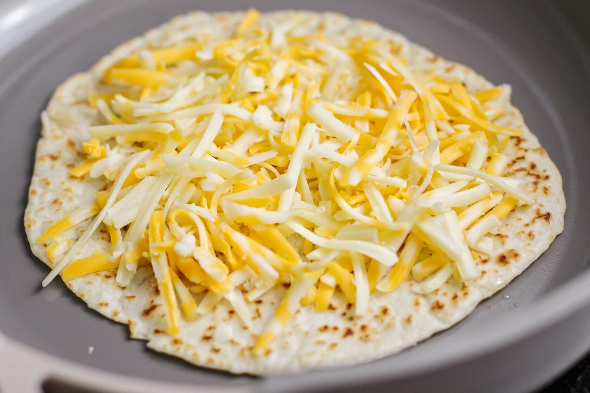 Shredded cheese on a tortilla in a pan.