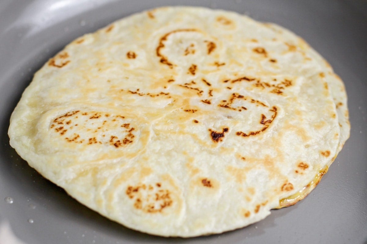 Browning a tortilla in a pan on the stove.