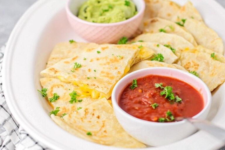 A cheese quesadilla sliced into triangles and served with cups of red and green salsa.