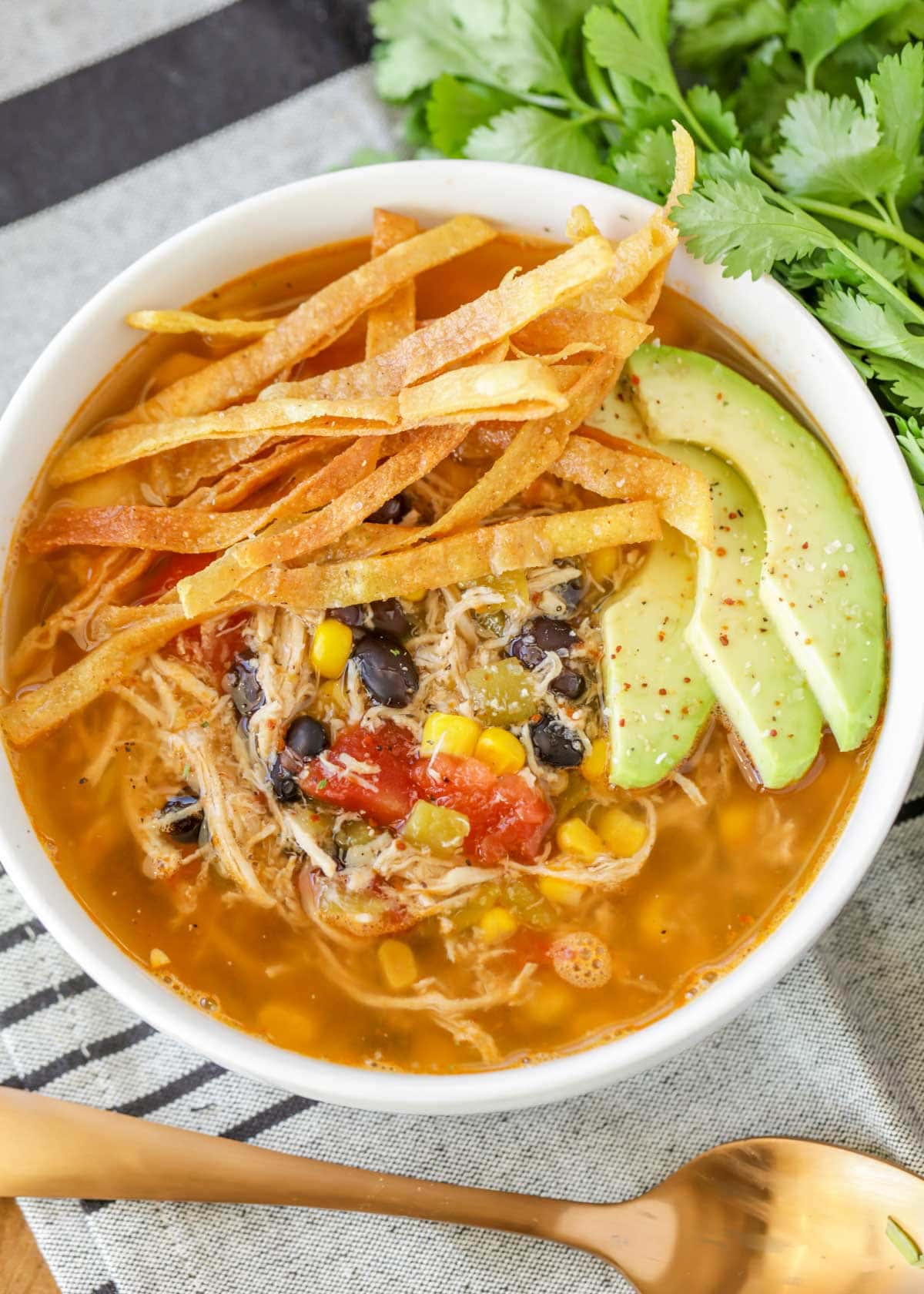 Chicken Tortilla Soup recipe in bowl with tortilla strips and avocado on top.
