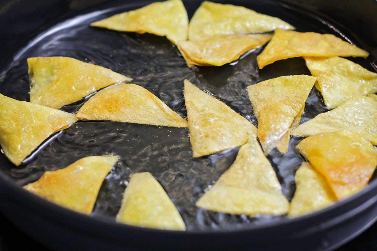 Frying tortilla triangles in a pan of oil.