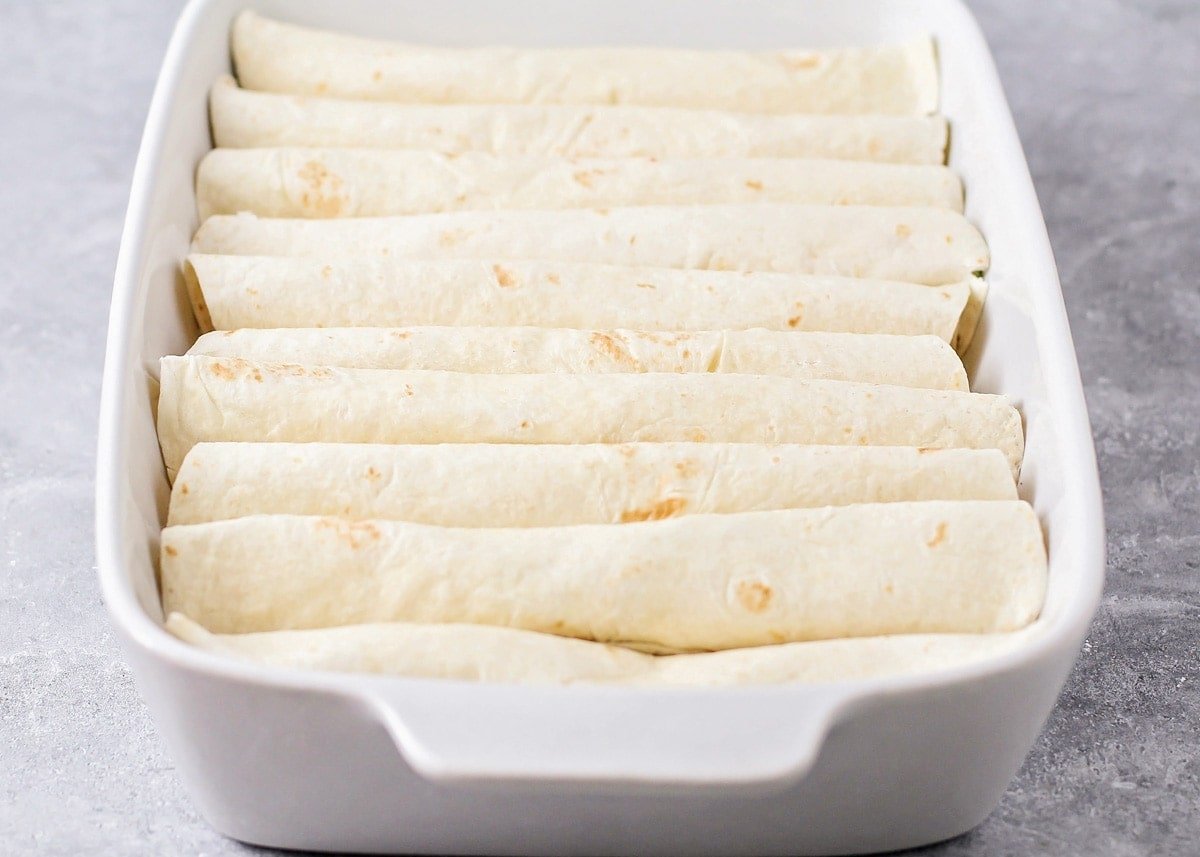 Filled flour tortillas rolled and lined up in a white baking dish.