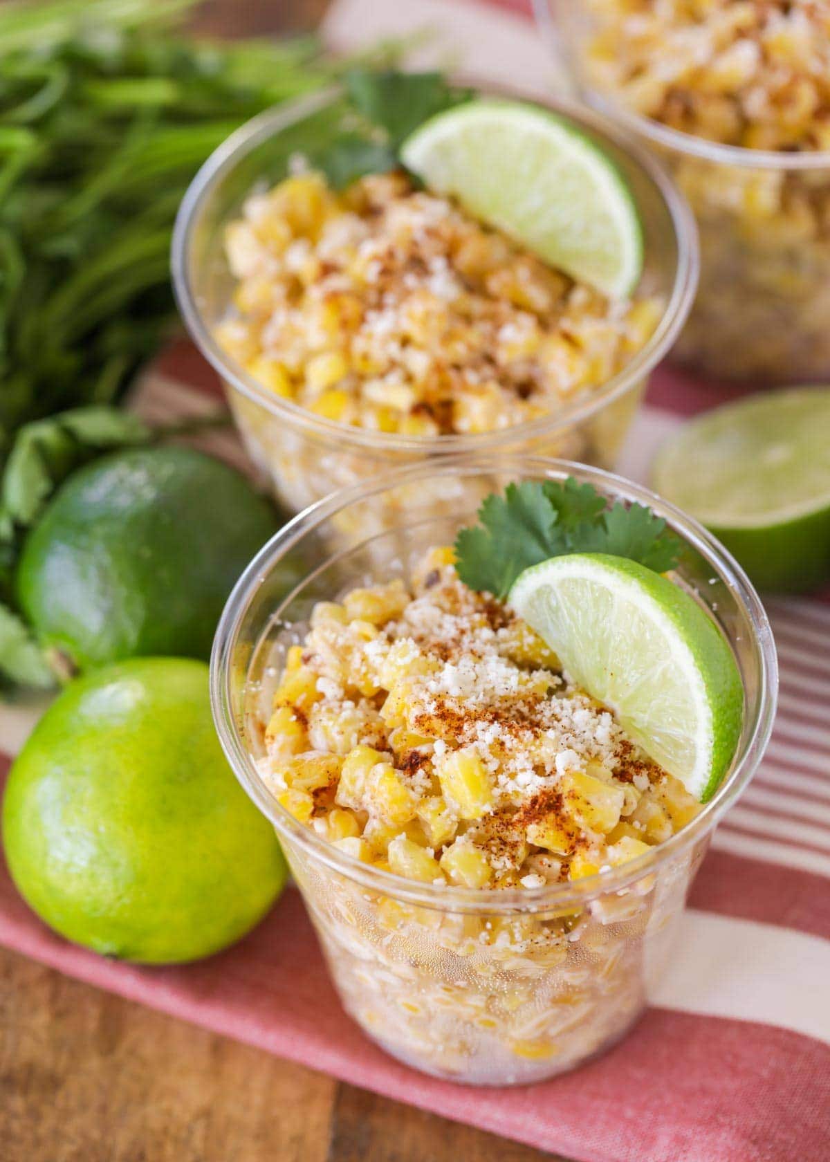 Corn esquites in a plastic cup with lime and cilantro.
