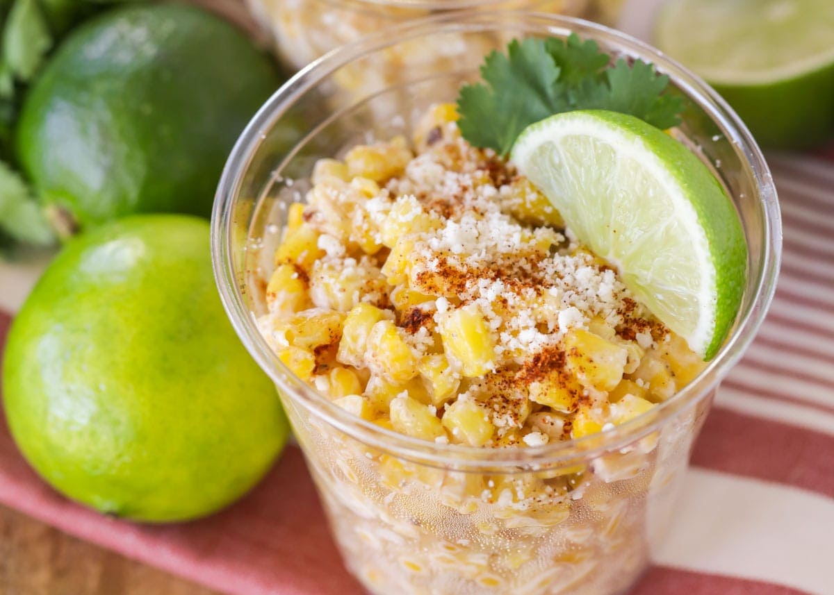 Esquites in a plastic cup with lime and cilantro.