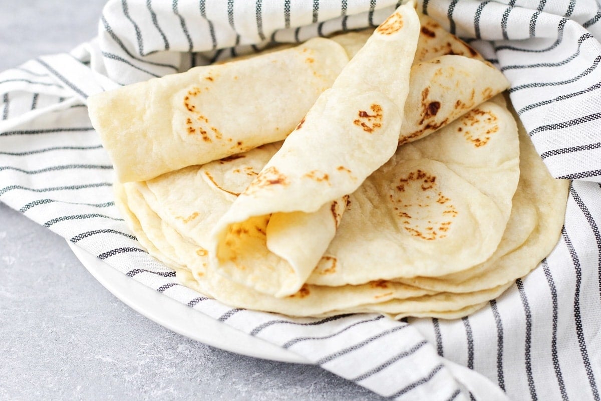 Flour tortilla rolled up on stack of tortillas.